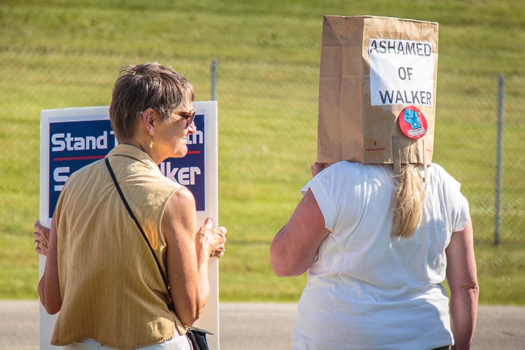 Not everyone in Waukesha was thrilled by Walker’s aspirations. A row of protestors, contained in a fenced area on the other side of the Expo Center’s parking lot, chanted and held signs. An airplane slowly trolled overhead towing a sign that read “Scott Walker has a Koch Problem.”