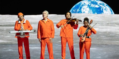 David Byrne and band in front of a moon backdrop